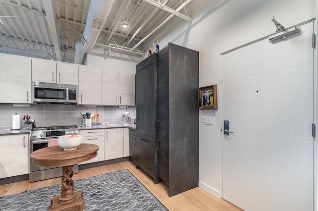 kitchen with light wood-type flooring, decorative backsplash, dark countertops, and stainless steel appliances