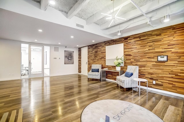 living area with wood walls, visible vents, an accent wall, beamed ceiling, and wood finished floors