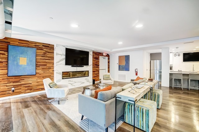 living room featuring a fireplace, visible vents, recessed lighting, wood finished floors, and wooden walls