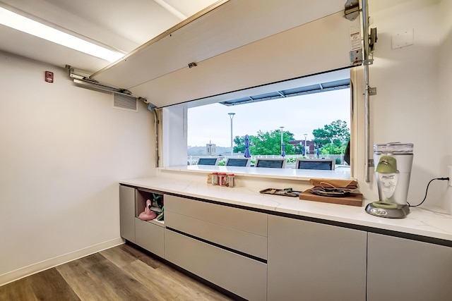 kitchen with modern cabinets, light stone countertops, white cabinetry, wood finished floors, and baseboards
