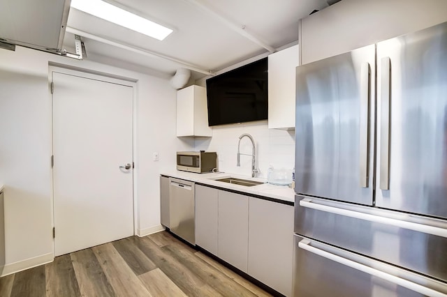 kitchen with white cabinetry, appliances with stainless steel finishes, wood finished floors, a sink, and decorative backsplash