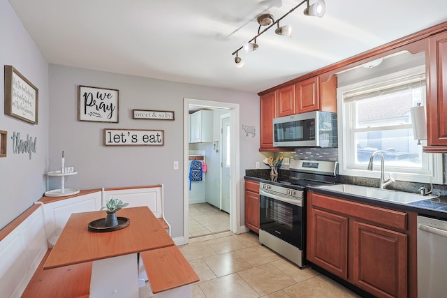 kitchen with light tile patterned floors, a sink, appliances with stainless steel finishes, dark countertops, and backsplash