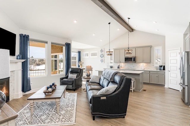 living area with beam ceiling, light wood-style floors, a glass covered fireplace, healthy amount of natural light, and high vaulted ceiling