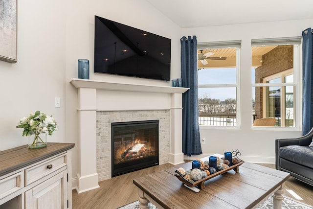 living area with a brick fireplace, wood finished floors, baseboards, and a ceiling fan
