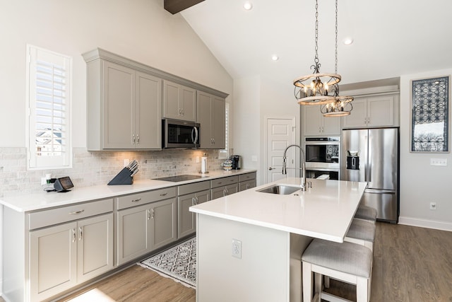 kitchen featuring gray cabinetry, stainless steel appliances, a sink, vaulted ceiling, and wood finished floors