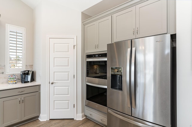 kitchen featuring appliances with stainless steel finishes, gray cabinets, decorative backsplash, light wood-style floors, and light countertops