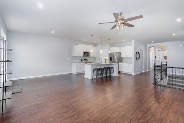 living room featuring arched walkways, dark wood-style flooring, baseboards, and a ceiling fan
