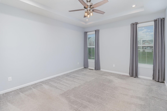 empty room with light colored carpet, a ceiling fan, a raised ceiling, baseboards, and recessed lighting