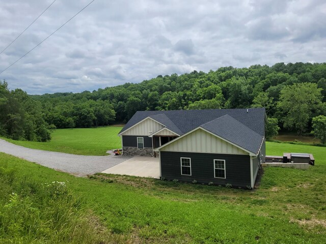 4400 Chipman Ridge Rd, Williamstown, KY 41097 - view of side of home featuring board and batten siding, a lawn, a shingled roof, a forest view, and a patio