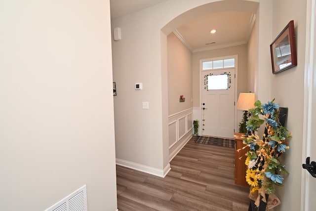foyer entrance with arched walkways, a decorative wall, crown molding, wainscoting, and wood finished floors
