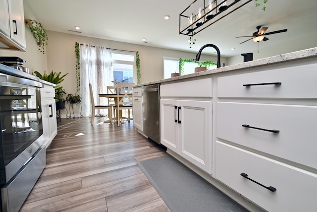kitchen featuring stainless steel dishwasher, light stone countertops, a ceiling fan, white cabinetry, and light wood finished floors