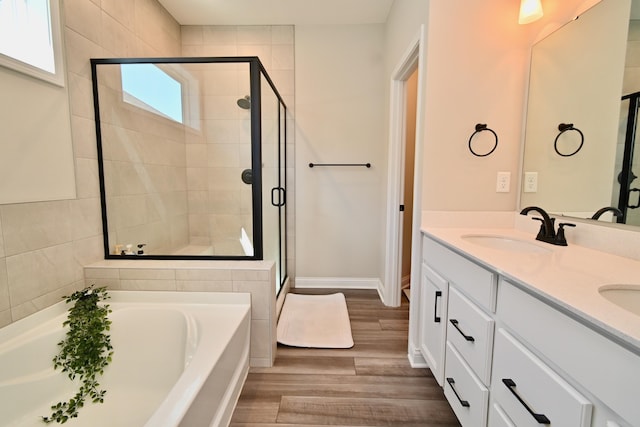 bathroom featuring double vanity, a stall shower, a bath, a sink, and wood finished floors