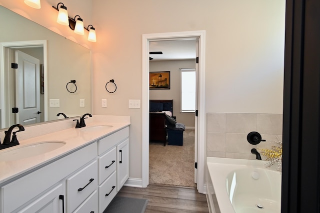 bathroom with a bath, wood finished floors, double vanity, and a sink