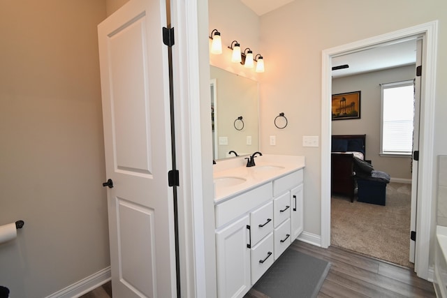 bathroom featuring double vanity, a sink, a bathtub, and baseboards