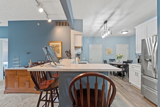 kitchen with a kitchen bar, stainless steel refrigerator with ice dispenser, visible vents, a sink, and white cabinetry