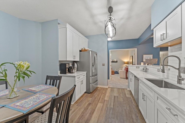 kitchen with decorative backsplash, a sink, light countertops, light wood-style floors, and white cabinetry