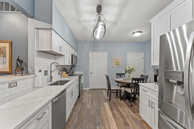 kitchen with a sink, stainless steel appliances, white cabinetry, wood finished floors, and backsplash
