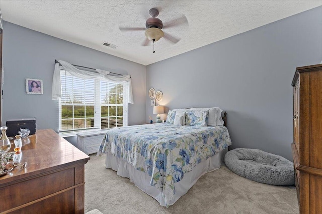 bedroom featuring visible vents, ceiling fan, a textured ceiling, and light colored carpet