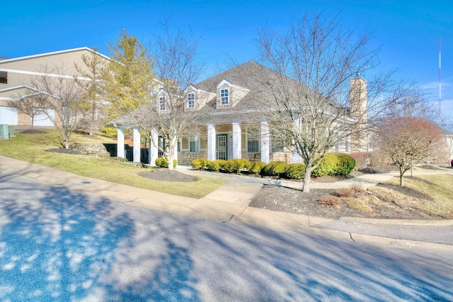 view of front facade featuring a porch, a front yard, a chimney, and stone siding