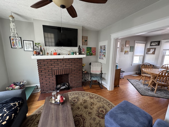 living area featuring a textured ceiling, a ceiling fan, wood finished floors, and a fireplace