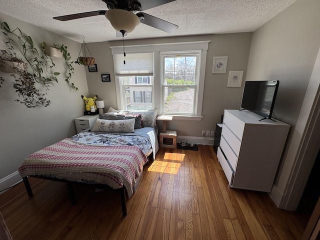 bedroom with baseboards, ceiling fan, hardwood / wood-style flooring, and a textured ceiling