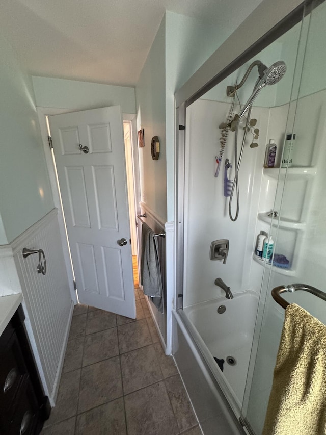 full bathroom with tile patterned floors, bath / shower combo with glass door, and a wainscoted wall