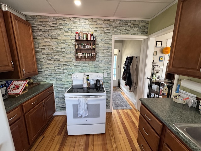 kitchen featuring crown molding, white range with electric cooktop, light wood-style flooring, a sink, and dark countertops