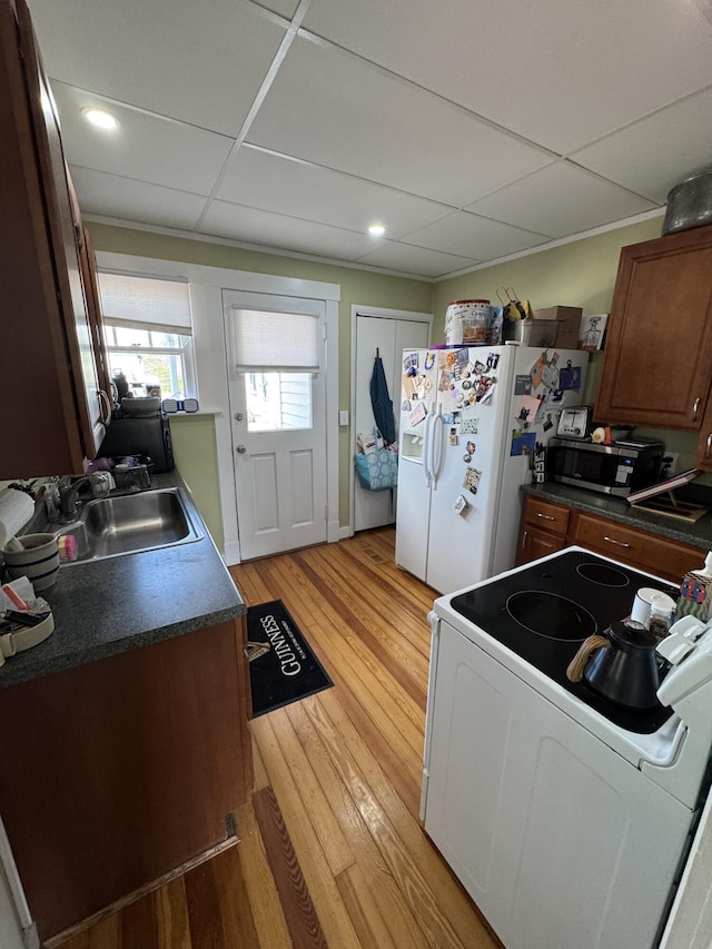kitchen with recessed lighting, white appliances, light wood-style flooring, dark countertops, and a sink
