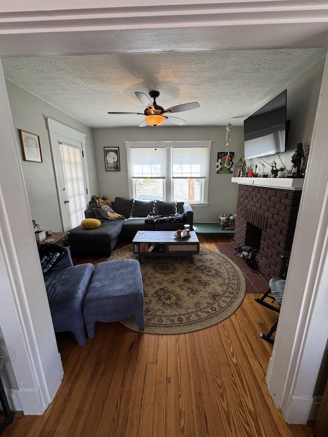 living room featuring a fireplace, ceiling fan, a textured ceiling, and wood finished floors
