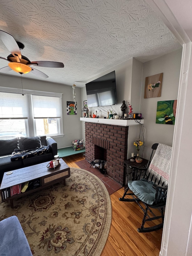 living room featuring a brick fireplace, ceiling fan, wood finished floors, and a textured ceiling