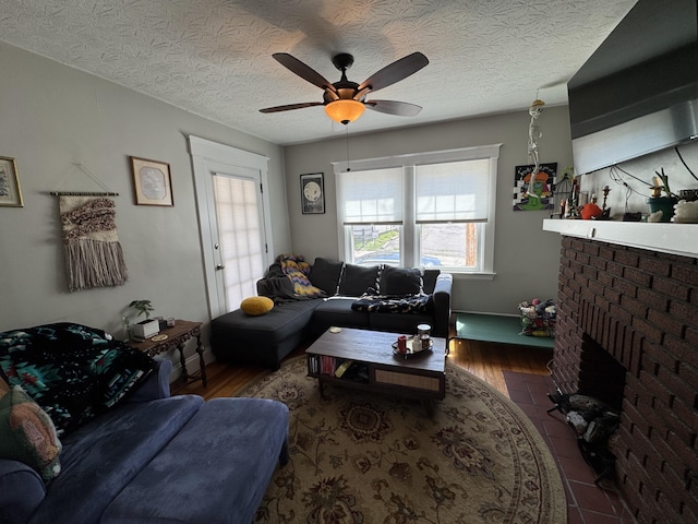 living room featuring a brick fireplace, a textured ceiling, wood finished floors, and ceiling fan