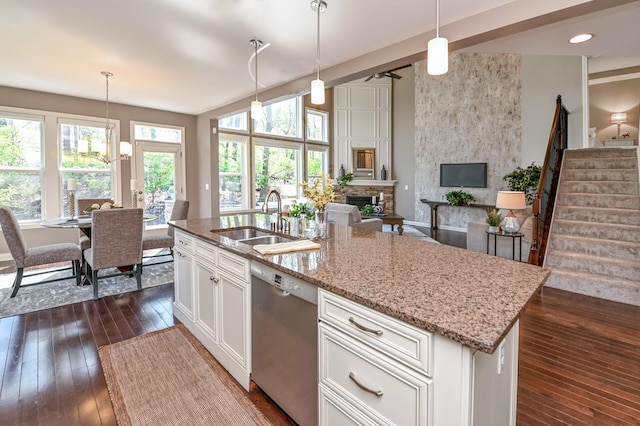 kitchen featuring dishwasher, a sink, a fireplace, dark wood finished floors, and light stone counters