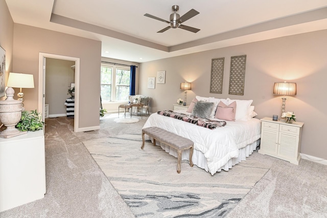 bedroom featuring baseboards, a walk in closet, a raised ceiling, and light carpet