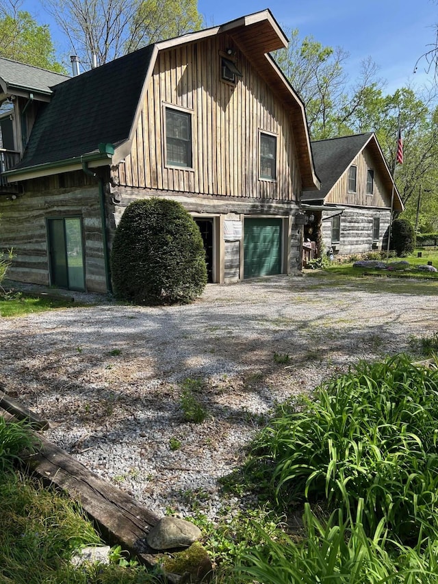 view of home's exterior with board and batten siding, roof with shingles, a gambrel roof, and gravel driveway