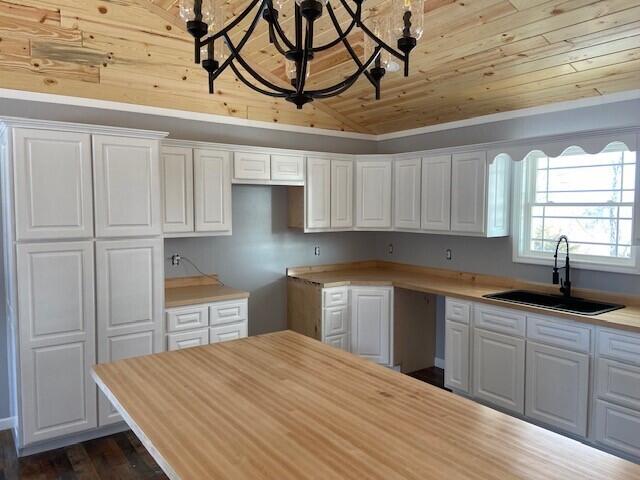 kitchen with a chandelier, wooden ceiling, a sink, and white cabinetry