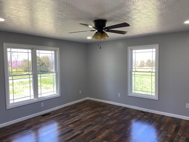 unfurnished room with dark wood-type flooring, a textured ceiling, baseboards, and visible vents