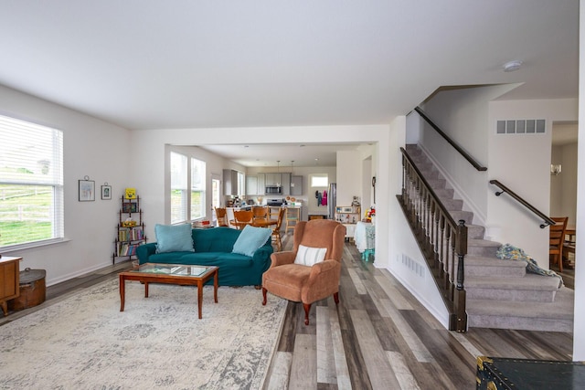 living room featuring visible vents, a healthy amount of sunlight, wood finished floors, and stairs