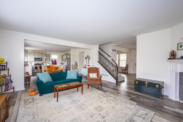 living room featuring a fireplace, visible vents, wood finished floors, stairs, and baseboards