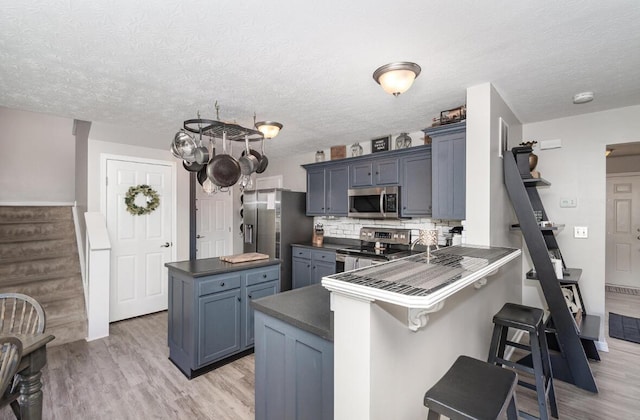 kitchen featuring a kitchen bar, a peninsula, light wood-style flooring, dark countertops, and stainless steel appliances