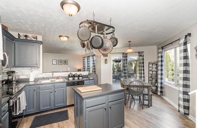 kitchen featuring light wood-type flooring, gray cabinets, a textured ceiling, appliances with stainless steel finishes, and a sink