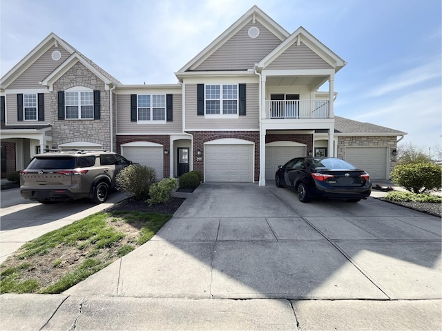 view of front of home featuring an attached garage, driveway, stone siding, and a balcony
