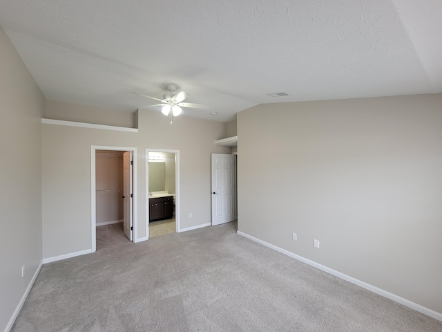 unfurnished bedroom featuring light carpet, ceiling fan, baseboards, and a walk in closet