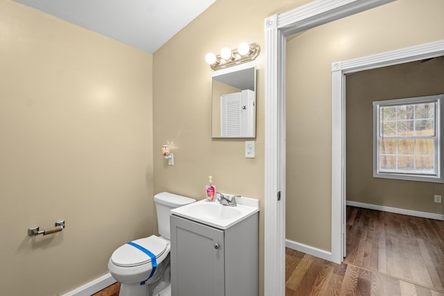 half bath featuring toilet, wood finished floors, vanity, and baseboards