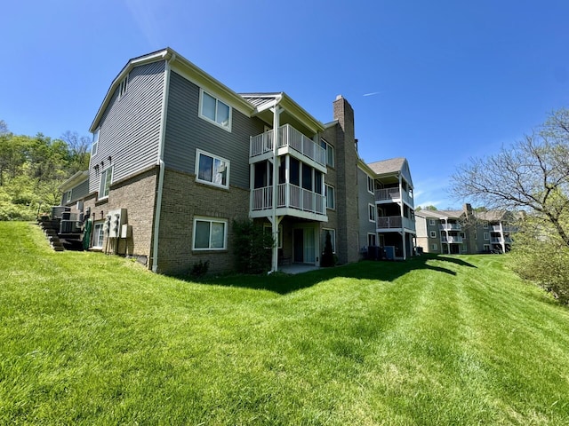 rear view of house with a lawn, a chimney, a balcony, and brick siding