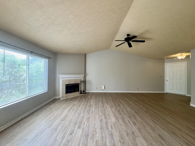 unfurnished living room featuring a textured ceiling, a ceiling fan, wood finished floors, a tile fireplace, and vaulted ceiling