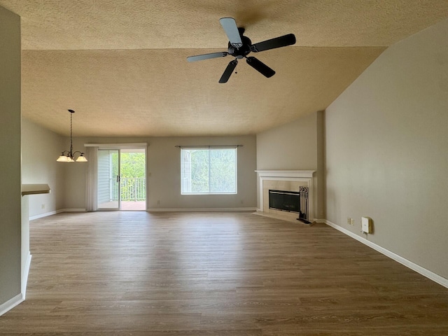 unfurnished living room featuring wood finished floors, baseboards, a textured ceiling, a tiled fireplace, and ceiling fan with notable chandelier