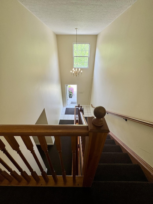 stairs featuring baseboards, a textured ceiling, and a notable chandelier