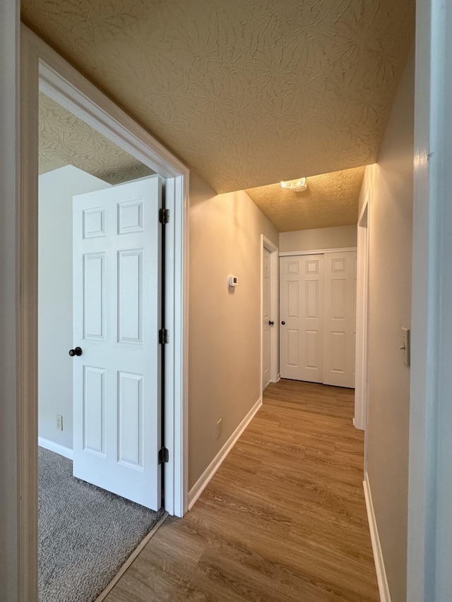 hall with baseboards, a textured ceiling, and wood finished floors