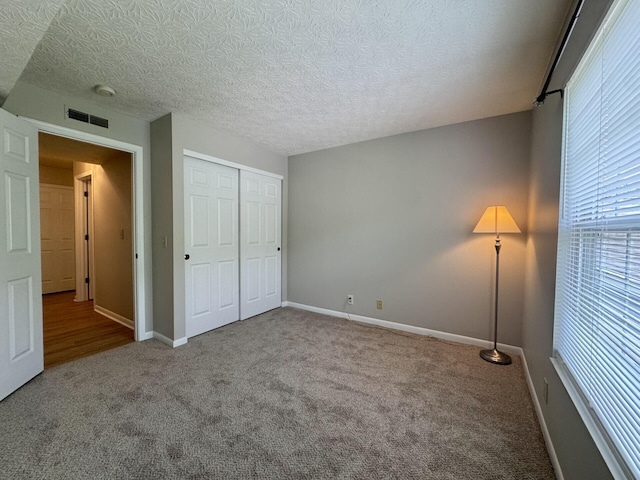 unfurnished bedroom with a textured ceiling, visible vents, baseboards, a closet, and carpet