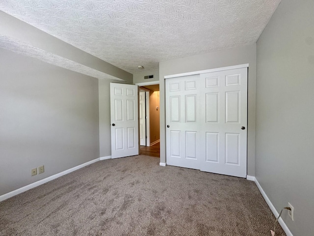 unfurnished bedroom featuring a textured ceiling, visible vents, carpet floors, baseboards, and a closet